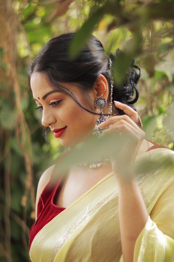 A young woman poses gracefully in a yellow saree and red blouse, showcasing traditional Indian fashion.