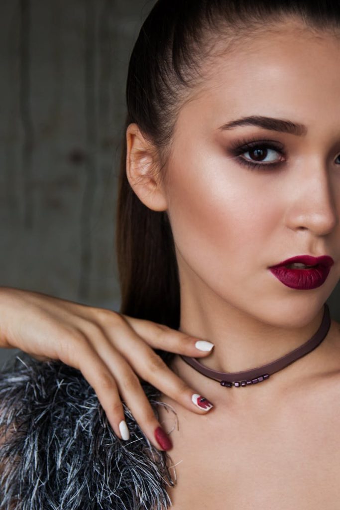 Close-up portrait of an elegant woman with bold makeup and fashionable attire, exuding confidence.