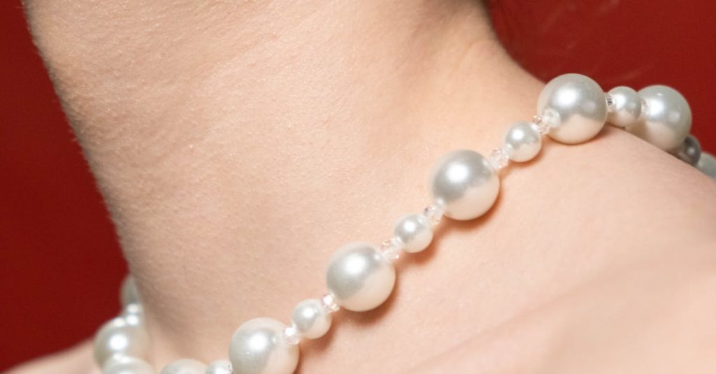 Close-up of a woman's neck adorned with a pearl necklace against a red background.