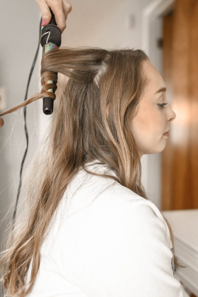 Profile of a woman having her hair curled with an iron in a salon setting.